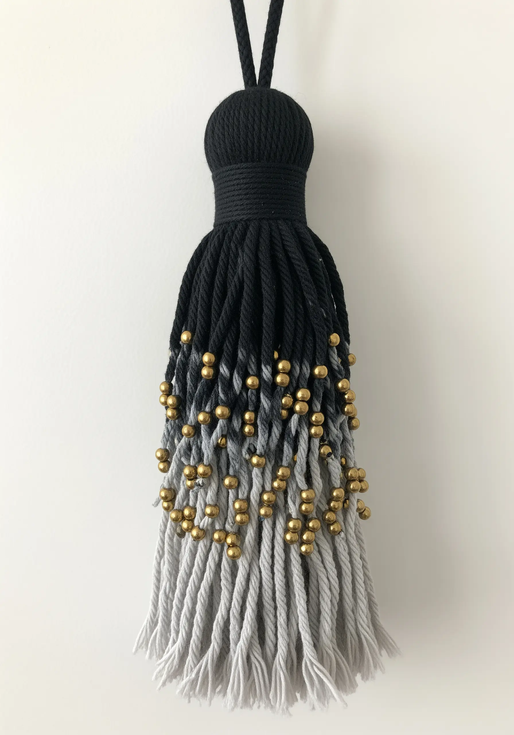 An oversized tassel with a black-to-grey gradient and scattered gold beads.