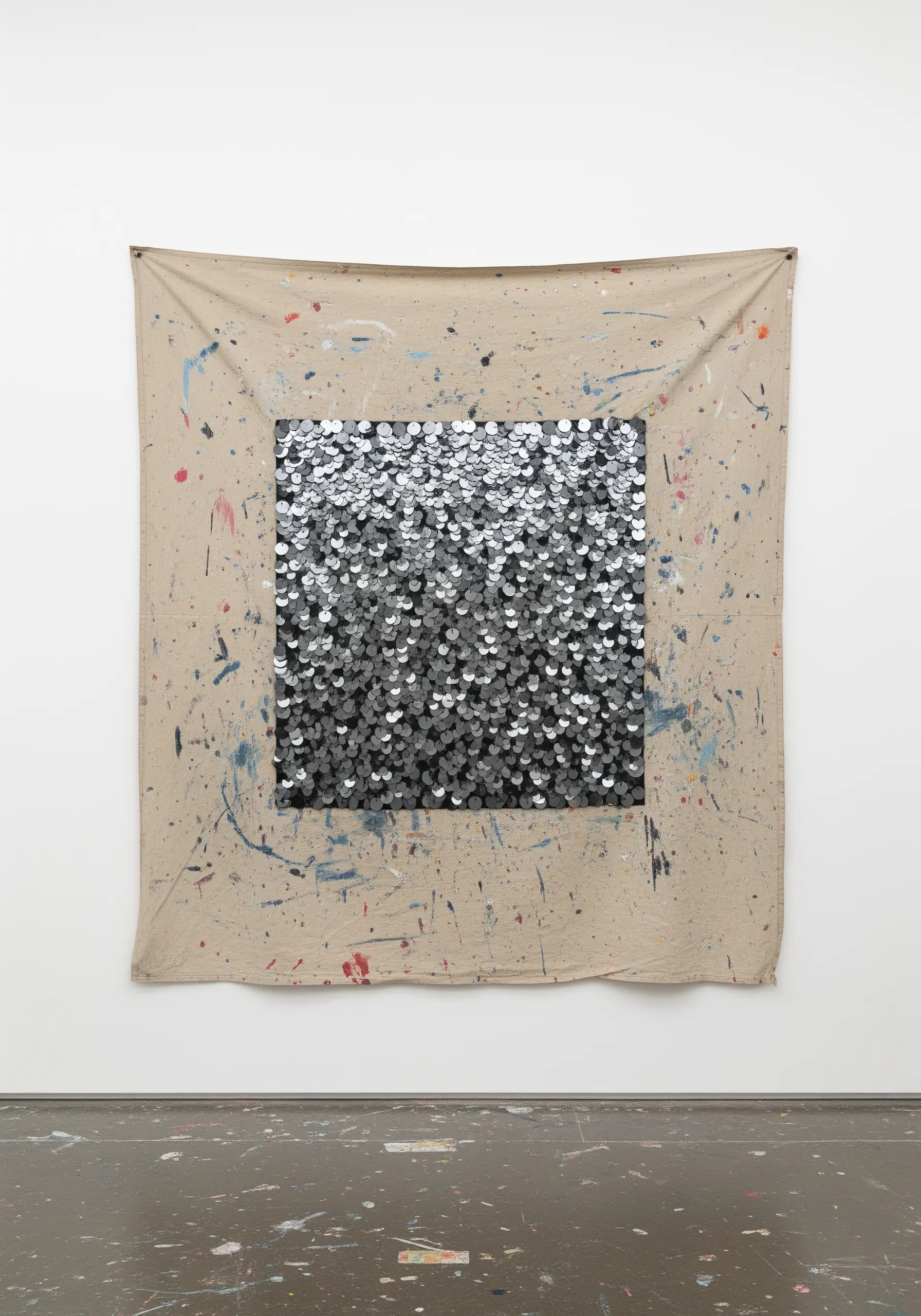A large, paint-splattered canvas with a dense, glittering square of silver sequins in the center.